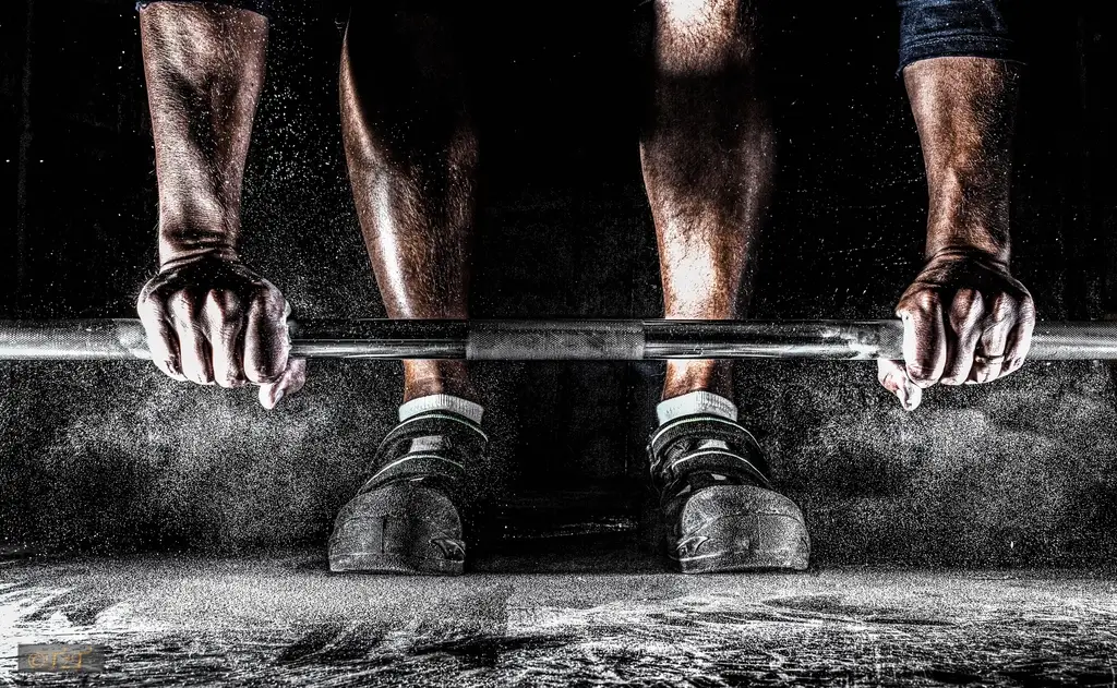 A lifter's chalked hands gripping a barbell on a gym floor before a deadlift