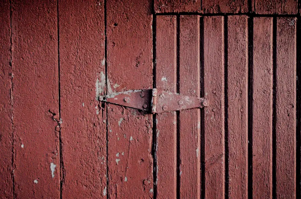 Before: a weathered red carriage-house door with peeling paint and a rusty strap hinge